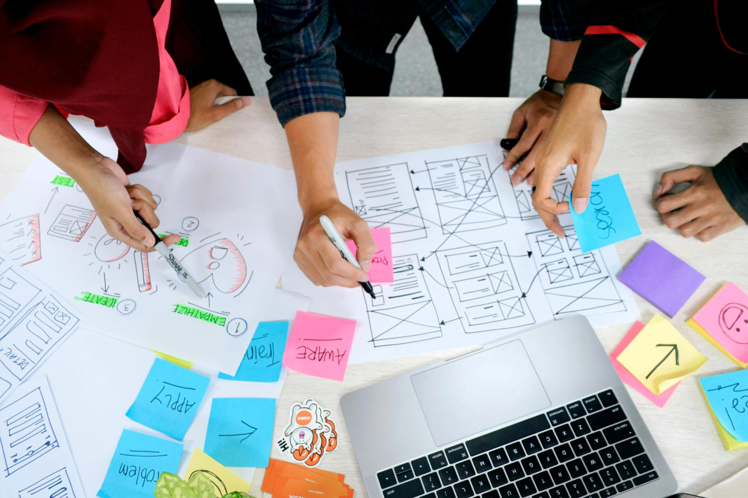 Bistrón web & email solutions service Three people collaborating on design blueprints and user experience wireframes with a laptop.